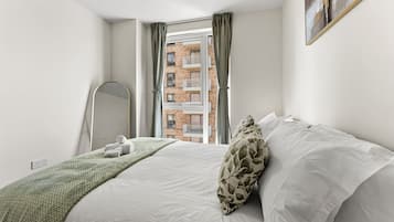 A bedroom with a bed, a mirror, a window with curtains, and a view of a building outside.