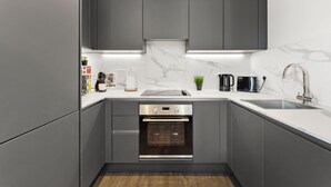 Eine moderne Küche mit grauen Schränken, einem Backofen, einer Spüle und einer Arbeitsplatte mit Kaffeemaschine und Toaster.