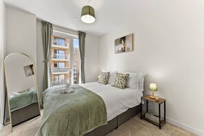 Une chambre à coucher avec un lit, une table de chevet avec une lampe, un miroir et une fenêtre avec des rideaux.