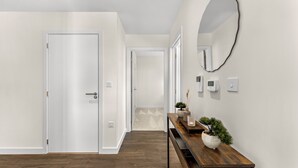 Ein Flur mit Holzboden, weißen Wänden, einer Holzbank mit Vase und Pflanzen sowie einem runden Spiegel an der Wand.