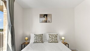 Ein Schlafzimmer mit einem Bett, zwei Nachttischen mit Lampen, einem Fenster mit Vorhängen und einem Bild an der Wand.