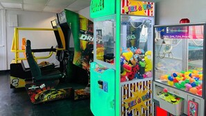 Ein Spielbereich mit verschiedenen Spielautomaten, darunter Rennspiele, Krabspelzmaschinen und Ballspiele.