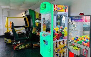 Ein Spielbereich mit verschiedenen Spielautomaten, darunter Rennspiele, Krabspelzmaschinen und Ballspiele.
