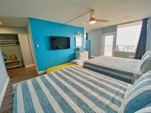 Ein Zimmer mit zwei Betten, einem Fernseher, einem Deckenventilator und einem Balkon mit Blick.