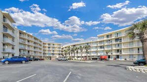 Ein mehrstöckiges Hotel mit Balkonen, einem Parkplatz und Palmen.