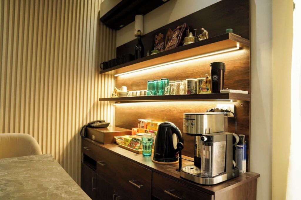 Une chambre d’hôtel avec un bureau en bois, une machine à café et une étagère contenant divers objets.