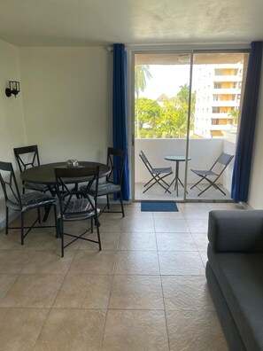A room with a dining table and chairs, a sofa, and a balcony with a view of buildings and trees. - Fresher Breeze, your home from home in the heart of the beautiful Ocho Rios (St Anns)