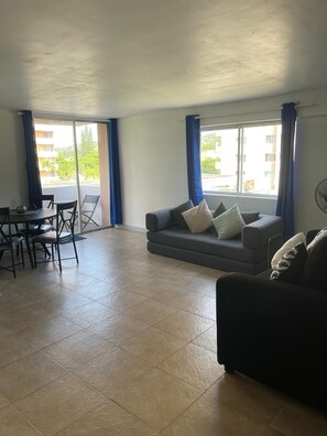 A spacious living area with a sofa, a dining table with chairs, and large windows with curtains. - Fresher Breeze, your home from home in the heart of the beautiful Ocho Rios (St Anns)