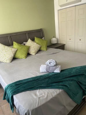 A neatly made bed with pillows, a rolled towel, and a green throw blanket. - Fresher Breeze, your home from home in the heart of the beautiful Ocho Rios (St Anns)