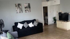A living room with a sofa, a TV on a stand, and a fan. - Fresher Breeze, your home from home in the heart of the beautiful Ocho Rios (St Anns)