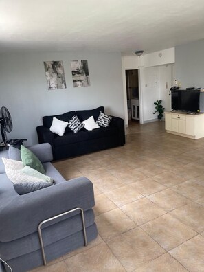 A living room with a sofa, a TV on a stand, and a fan. - Fresher Breeze, your home from home in the heart of the beautiful Ocho Rios (St Anns)