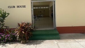 A building labeled 'CLUB HOUSE' with a green carpeted entrance, a glass door, and a small outdoor area with plants. - Fresher Breeze, your home from home in the heart of the beautiful Ocho Rios (St Anns)