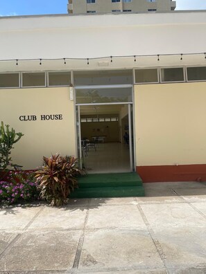 A building labeled 'CLUB HOUSE' with a green carpeted entrance, a glass door, and a small outdoor area with plants. - Fresher Breeze, your home from home in the heart of the beautiful Ocho Rios (St Anns)