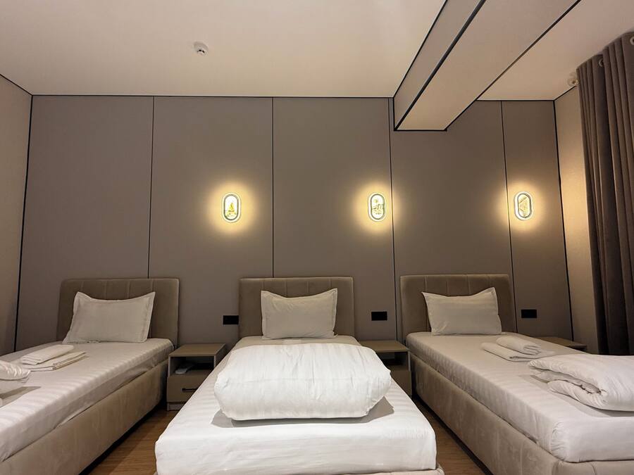 A hotel room with three single beds, a nightstand, a wall-mounted light fixture, and a framed picture on the wall.