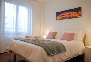A hotel room with a bed, pillows, a blanket, a painting on the wall, and a window with curtains. - Double Space Apartment - Milan - 6 guests · Airport · Train · Garage (Milano)