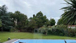 A swimming pool with a wooden deck, surrounded by lush greenery and trees. - Large house with a pool and spacious grounds in La Rochelle. (La Rochelle)