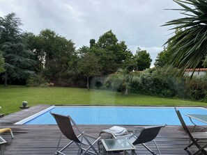 Ein Schwimmbecken mit Holzterrasse, umgeben von üppiger Vegetation und Bäumen.