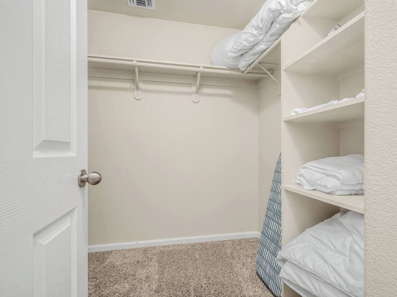 A walk-in closet with a door, a hanging rod, and shelves with folded towels.