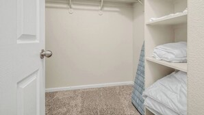 A walk-in closet with a door, a hanging rod, and shelves with folded towels. - Amber Cove Cottage - 3BR, 2BA, sleeps 8 (Fresno)
