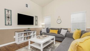 A living room with a flat-screen TV, a sofa, a coffee table, and a bookshelf. - Amber Cove Cottage - 3BR, 2BA, sleeps 8 (Fresno)
