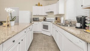 A modern kitchen with white cabinets, a granite countertop, a built-in oven, a microwave, a coffee maker, and a sink. - Amber Cove Cottage - 3BR, 2BA, sleeps 8 (Fresno)