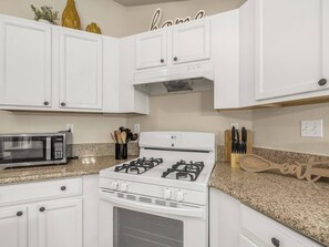 A kitchen with white cabinets, a gas stove, a microwave, and a knife block.