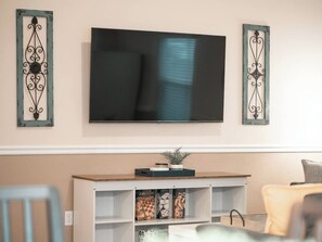 Un salon doté d’un téléviseur à écran plat fixé au mur, d’un meuble de rangement blanc contenant des jeux de société et de luminaires décoratifs fixés aux murs.