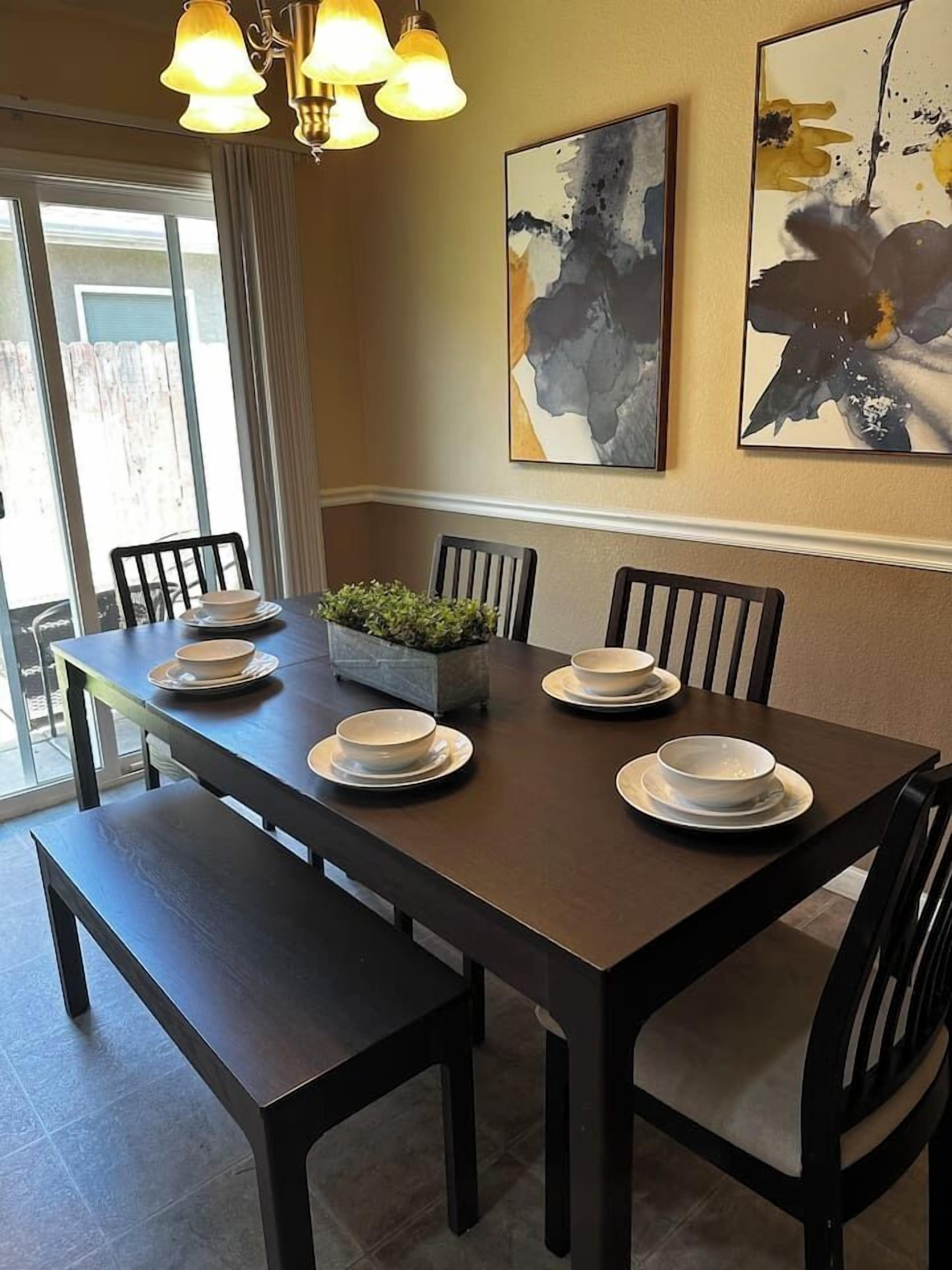 A dining area with a dark wooden table, white plates, and a small plant centerpiece.