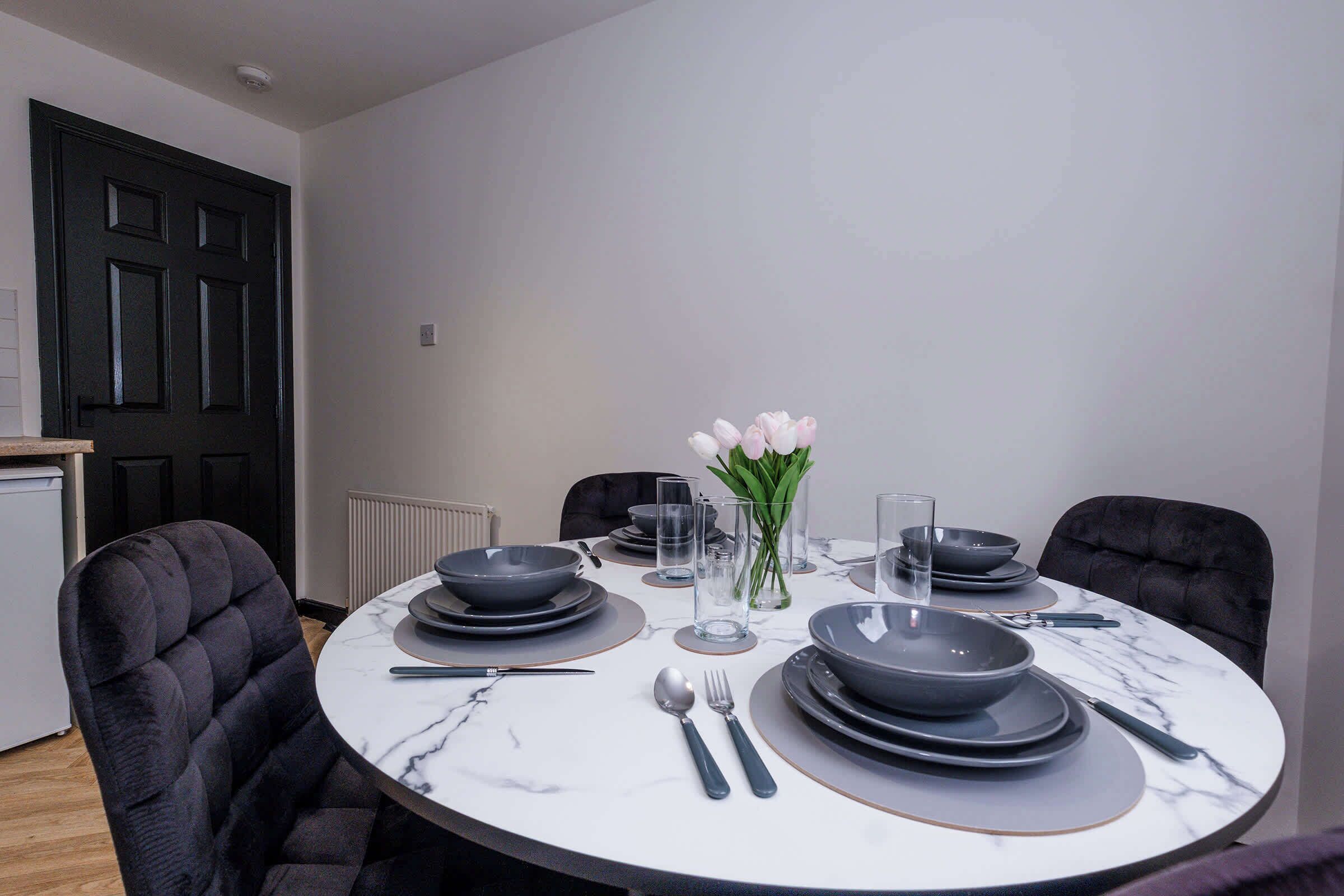 A dining table set with plates, bowls, cutlery, and glasses, surrounded by upholstered chairs.