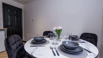 A dining table set with plates, bowls, cutlery, and glasses, surrounded by upholstered chairs.
