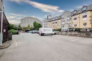 Ein Parkplatz mit einem weißen Lieferwagen im Vordergrund, umgeben von mehrstöckigen Wohngebäuden mit Balkonen.