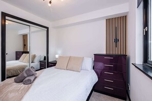 Ein Schlafzimmer mit Bett, Kommode, Spiegel und Fenster.