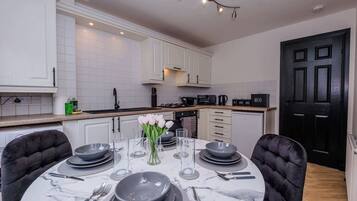 A modern kitchen with white cabinets, a black door, and a dining area set for six with plates, bowls, and cutlery.