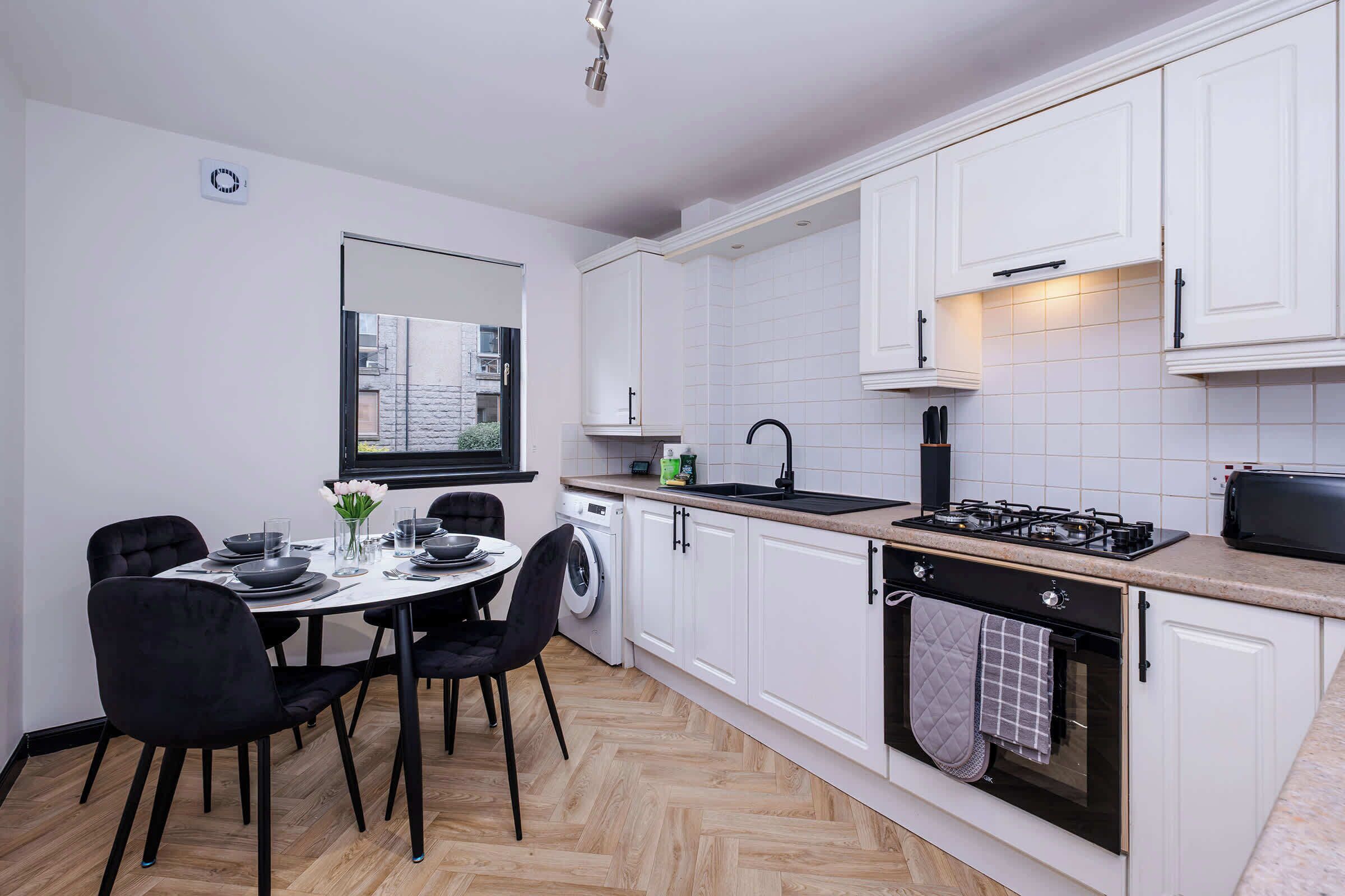Una cucina moderna con mobili bianchi, un'area pranzo con un tavolo rotondo e sedie, e una finestra.