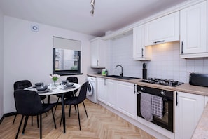Eine moderne Küche mit weißen Schränken, einem Essbereich mit rundem Tisch und Stühlen sowie einem sichtbaren Fenster.