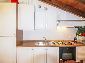 Cuina amb armaris blancs, un rentapeus d'acer inoxidable, fogó a gas i màquina d'esbandir plats.