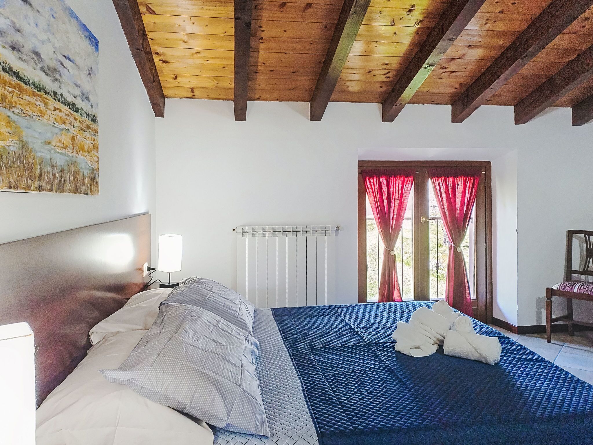 Une chambre à coucher avec un lit, une table de chevet, une fenêtre avec des rideaux et un tableau accroché au mur.