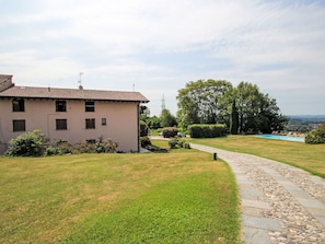 A residential property with a paved driveway leading to a swimming pool, surrounded by well-maintained lawns and mature trees. - Natalina by Interhome (Cocquio Trevisago)
