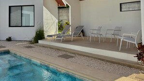 Uma área moderna com piscina ao ar livre, teto de madeira, paredes brancas e espreguiçadeiras.