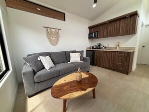 Ein modernes Wohnzimmer mit grauem Sofa, Couchtisch aus Holz und eingebauten Küchenschränken.