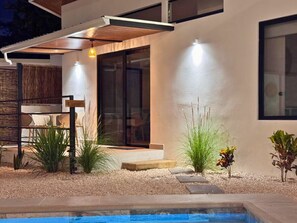 Ein moderner Poolbereich im Freien mit minimalistischem Design, inklusive einer Pergola, einer Sitzgelegenheit und einem gepflegten Garten.