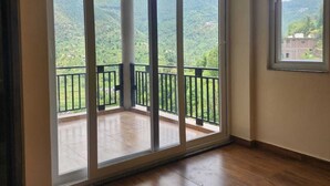 Quarto com uma grande porta de vidro deslizante que dá para uma varanda com vista para colinas verdes.