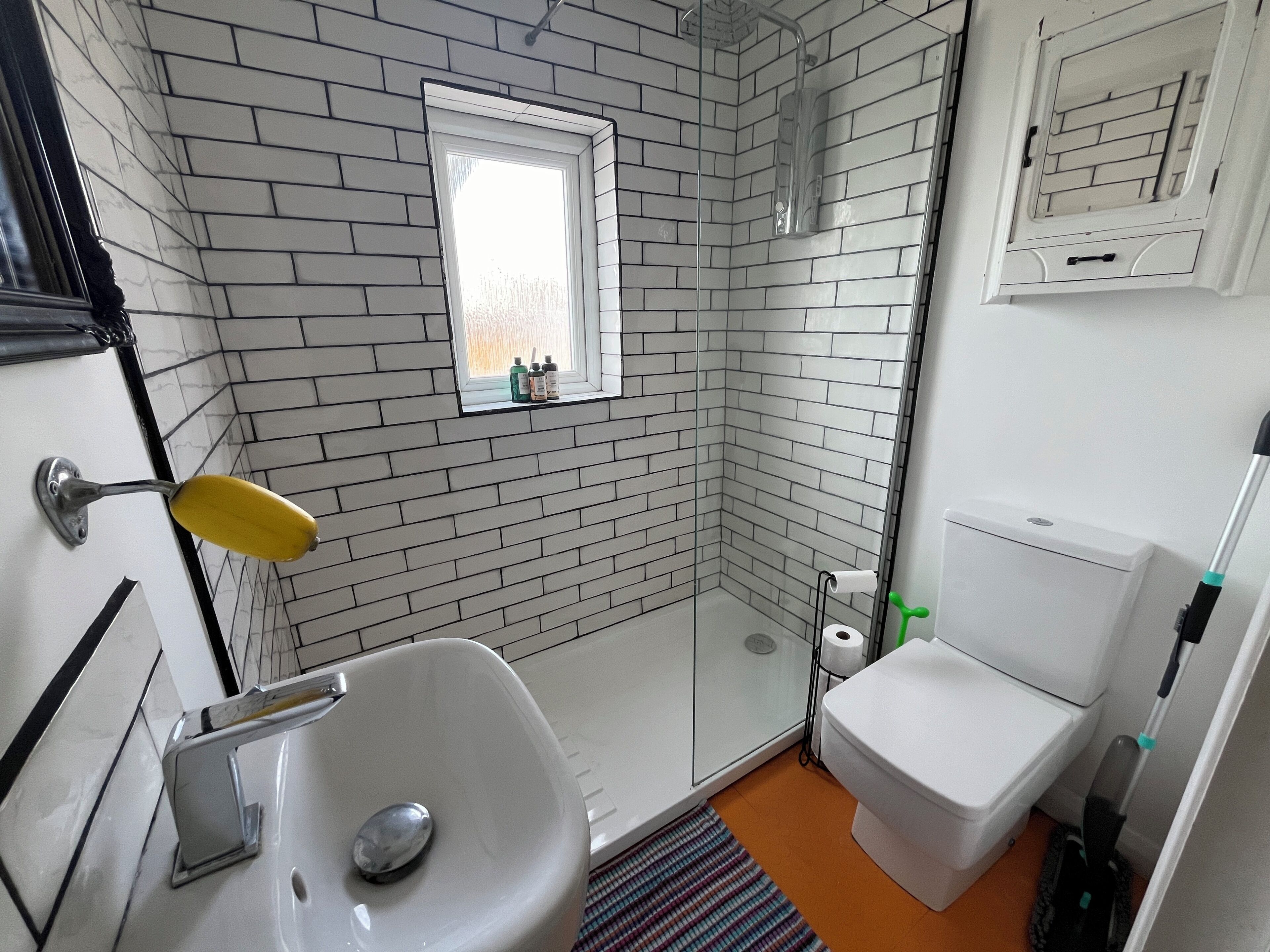 Un bany amb un lavabo blanc, una dutxa amb envàs de vidre, un vàter i una finestra amb vista.