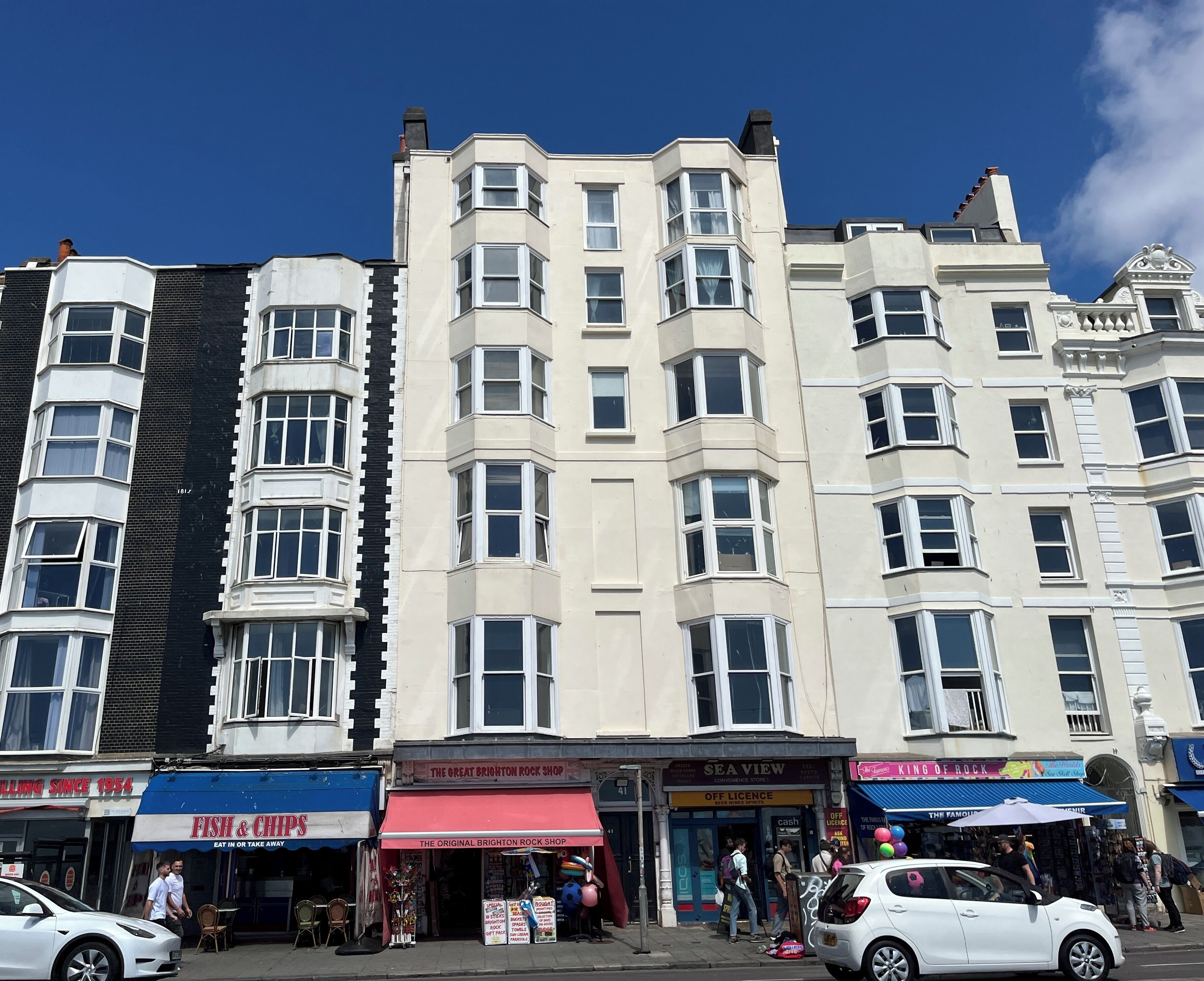A multi-story building with various shops on the ground floor, including a fish and chips restaurant and a rock shop.