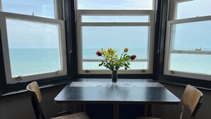 Ett rum med ett bord och två stolar, ett fönster med utsikt över havet och en vas med blommor på bordet.