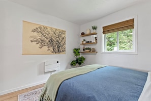 A bedroom with a bed, a wall-mounted thermostat, a window with blinds, and a wall-mounted shelf with books and decorative items. - Redwoods Adventure Home Base & Short Stroll to Ocean - The Boho Bungalow (Crescent City)
