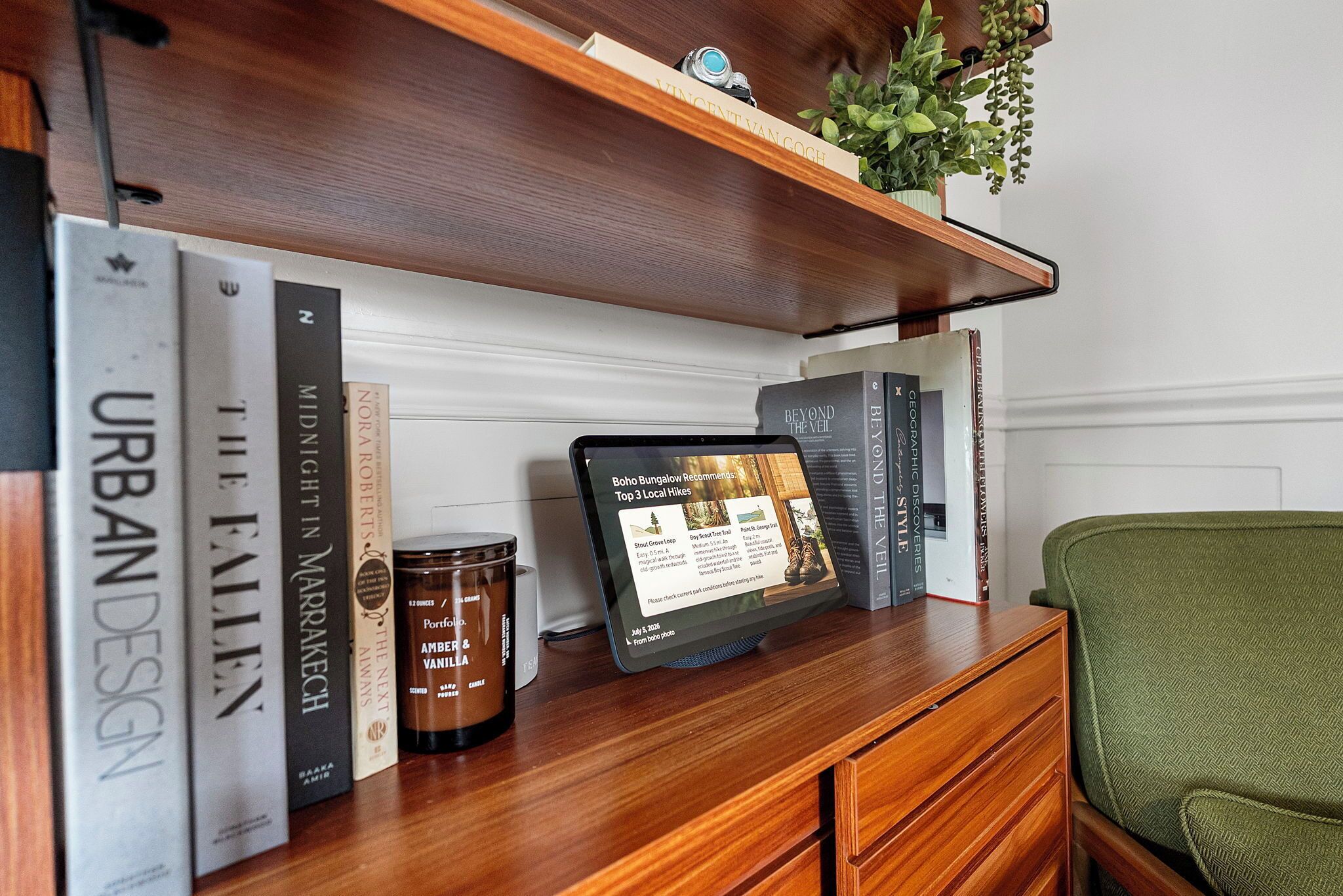 A wooden shelf with books, a candle, and a tablet displaying a hiking recommendation.