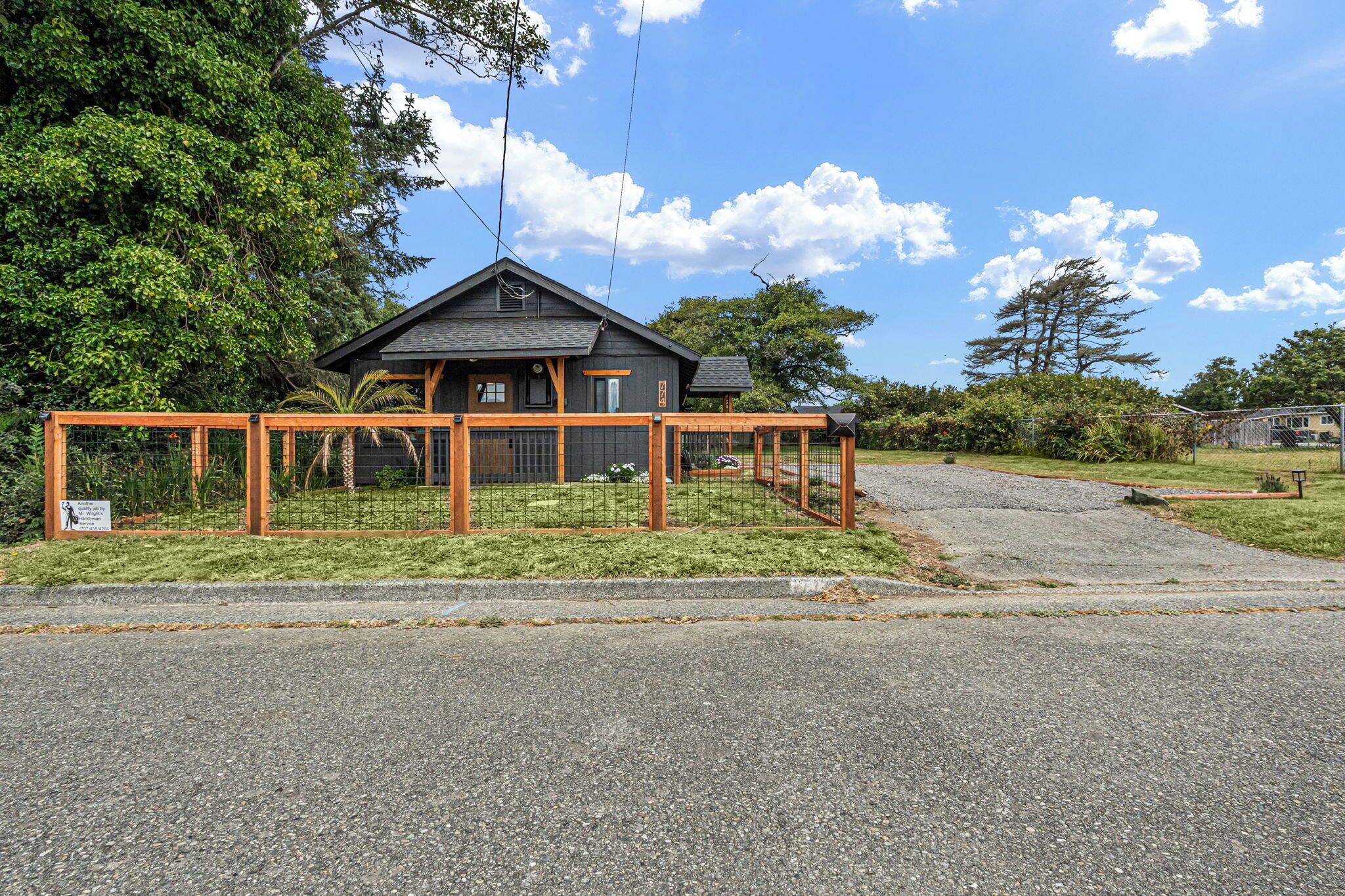 A two-story house with a fenced outdoor area, a gravel driveway, and a clear sky.
