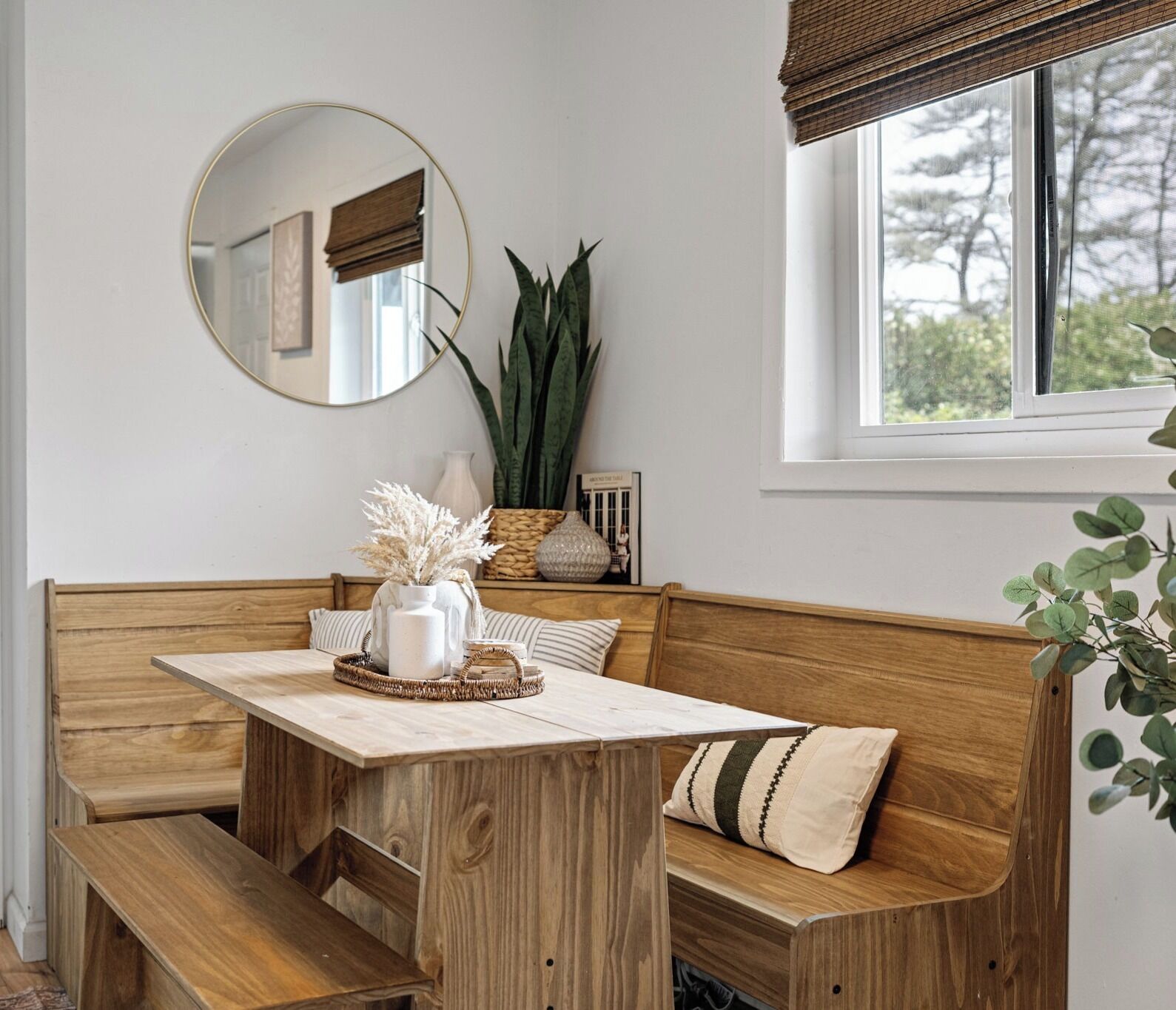 A wooden bench with a table, a mirror, and a window with a view of trees.