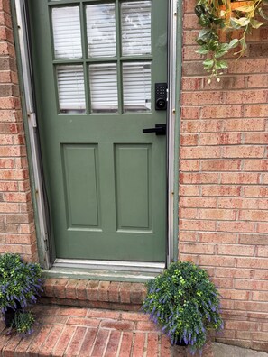 A green door with a keypad lock, a window with blinds, and a brick wall. - Gorgeous 3-bedroom bungalow with Hot Tub, Games and AC in Southern Pines (Southern Pines)